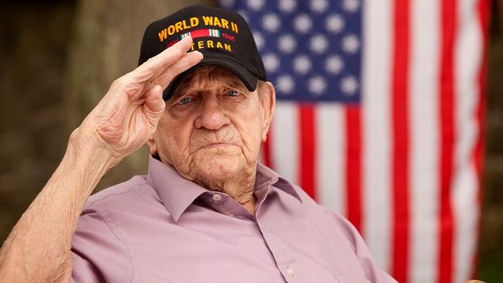A disabled World War II veteran salutes in front of an American flag. 